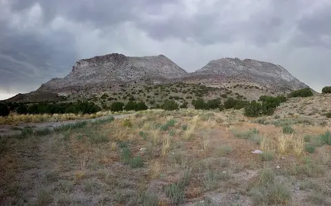 A view of rocky mountains and sparse vegetation under a cloudy sky.