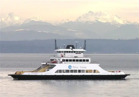A ferry is on the water with snowy mountains in the background.