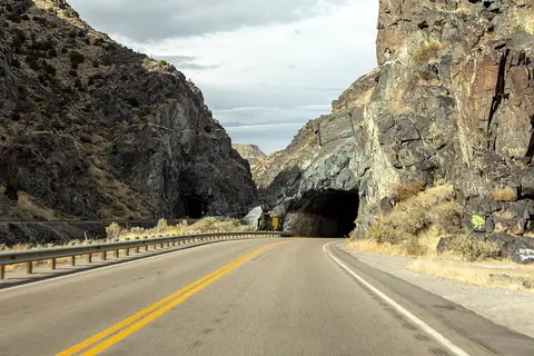 A paved road curves toward a tunnel carved through rocky cliffs.