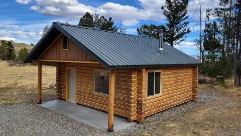 A log cabin stands in a rural landscape under a cloudy sky.