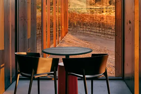 A table and two chairs inside a room with a large window looking out at a vineyard.