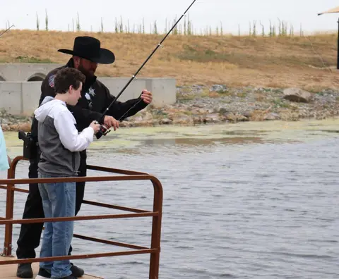 A young person and a law enforcement officer fish from a dock.