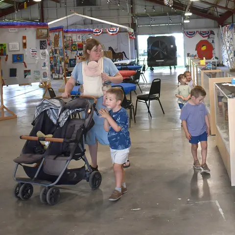A woman with a stroller and children walks through a large hall with displays.