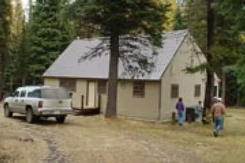 A single story building situated in a forest with a truck and people nearby.