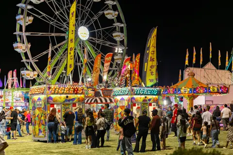 A night view of a carnival with a Ferris wheel and ticket booths.