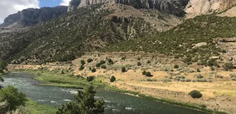 A river flows through a dry valley beneath steep mountains.