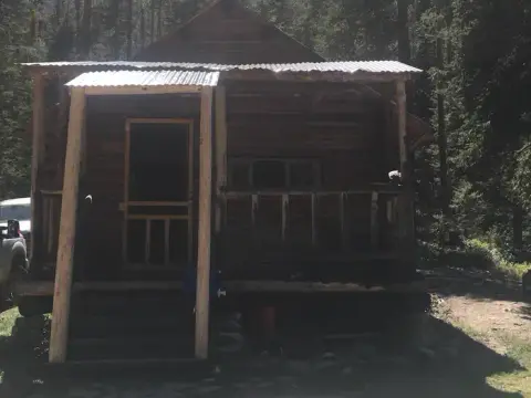 A rustic wooden cabin with a porch stands among trees.