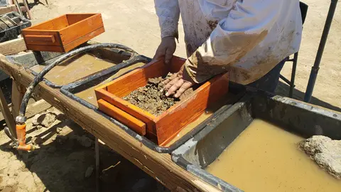A person washes and sifts dirt and rocks in a wooden sluice box.