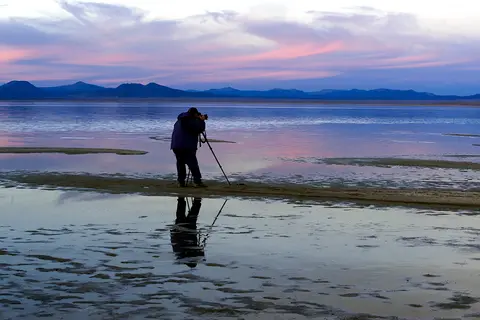 A photographer taking pictures of a scenic lake landscape at sunset.