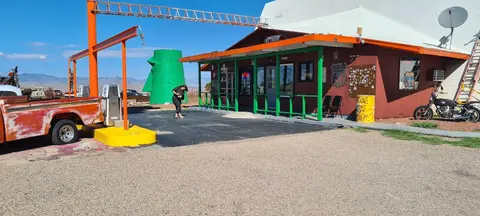 Exterior view of a roadside building with an orange and green porch, an old truck, and a person outside.