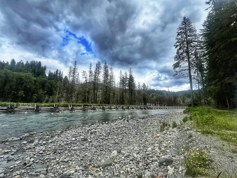 A rocky riverbank alongside a flowing river under a cloudy sky.