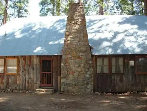 A rustic wooden cabin featuring a prominent stone chimney in the middle.