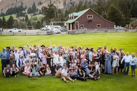 A large group of people posing for a photo on a lawn in front of a barn.