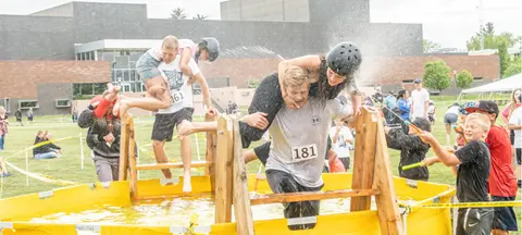 People participate in an outdoor obstacle course involving water.