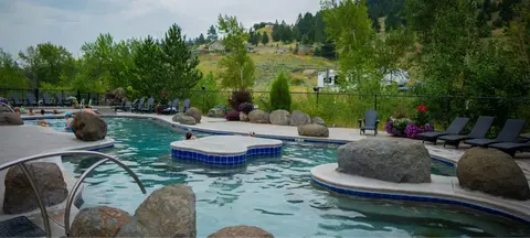 An outdoor swimming pool surrounded by rocks, loungers, and hills.