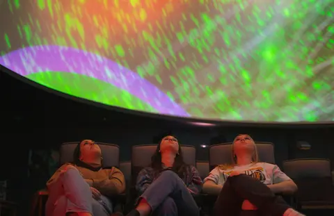Three people sitting in a theater looking up at a dome screen.