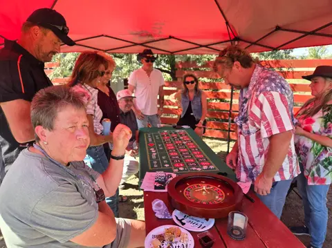A group of people gathered around a roulette table under a red canopy.