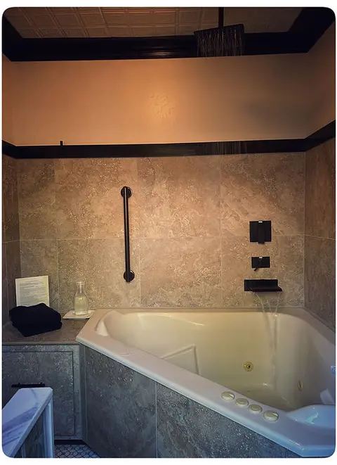 A corner bathtub with tiled walls and a shower fixture above.