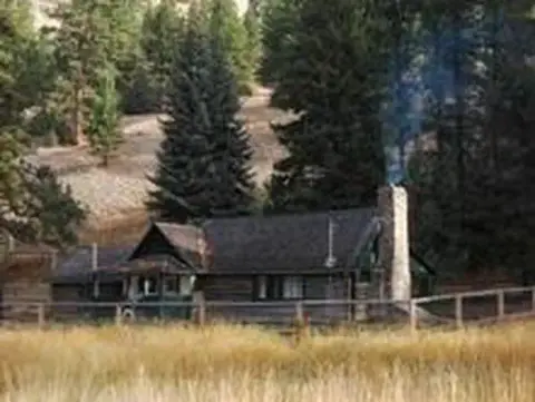 A log cabin sits among trees with smoke rising from its stone chimney.