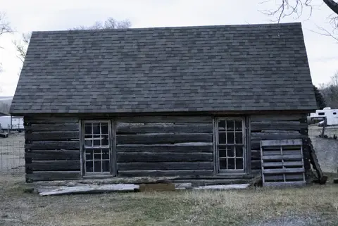 Exterior view of a dark log building with a shingled roof and two windows.