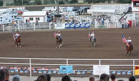 Four horse riders carrying American flags in an arena during a rodeo event.