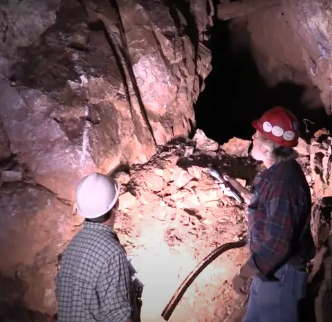 Two people in hard hats explore a dark mine shaft.