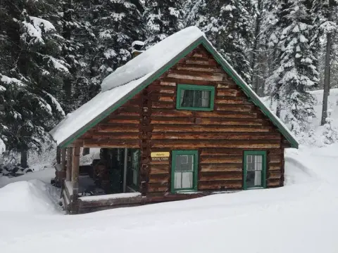 A log cabin covered in snow in a forest.