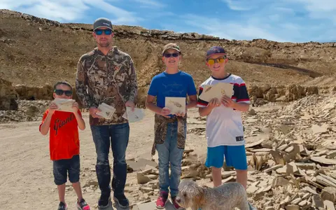 Four people and a dog pose in an outdoor quarry holding fossils.