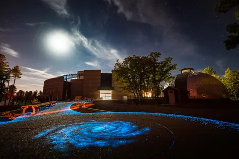 A nighttime exterior view of a modern building with a glowing galaxy path and a dome under a starry sky.