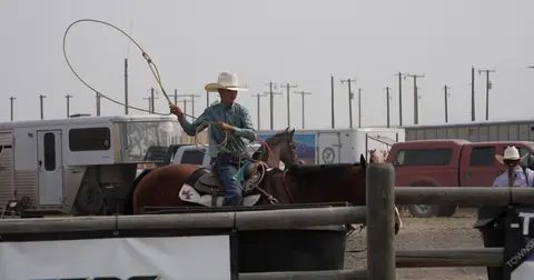 A cowboy on horseback prepares to throw a lasso.