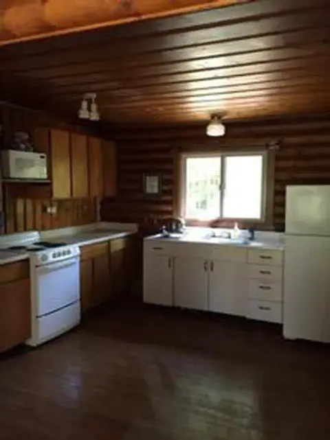 Interior view of a rustic log cabin kitchen with wooden walls and ceiling.