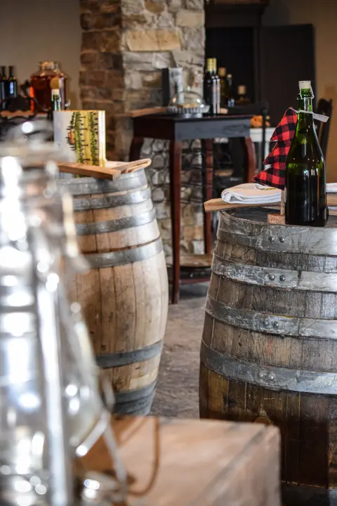 Wooden wine barrels stand inside a room with stone pillars and bottles of wine.