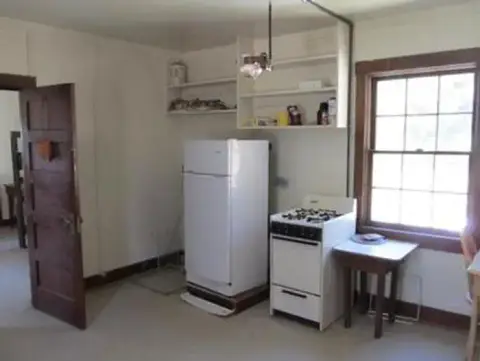 This photo shows the interior of a kitchen with a refrigerator, stove, and open shelving.