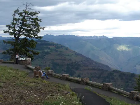 A scenic overlook with a paved path, a bench, and a view of mountains and valleys under a cloudy sky.