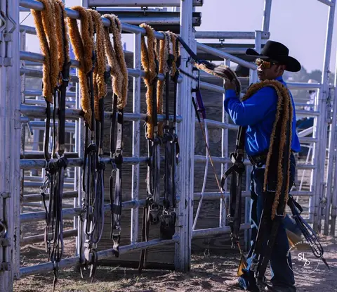 A cowboy prepares gear by metal gates.