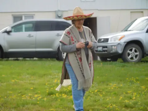 A person wearing a sombrero and poncho walks across a grassy area.