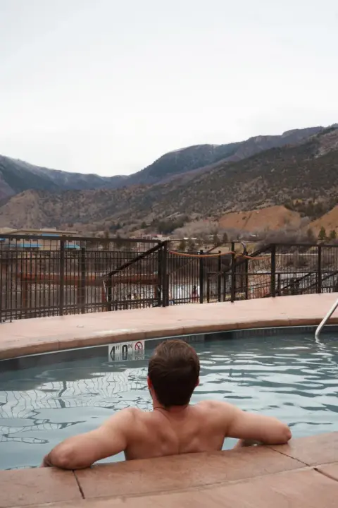 A person relaxes in an outdoor pool overlooking mountains.