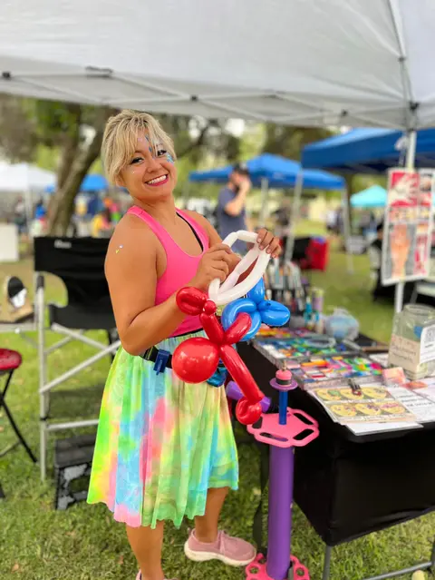 A woman holds balloon animals at an outdoor event booth.