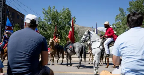 People ride horses in a parade as spectators watch from the foreground.