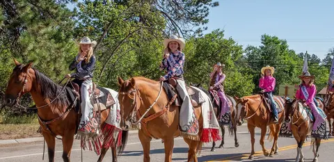 Several young people ride horses down a road during a parade event.