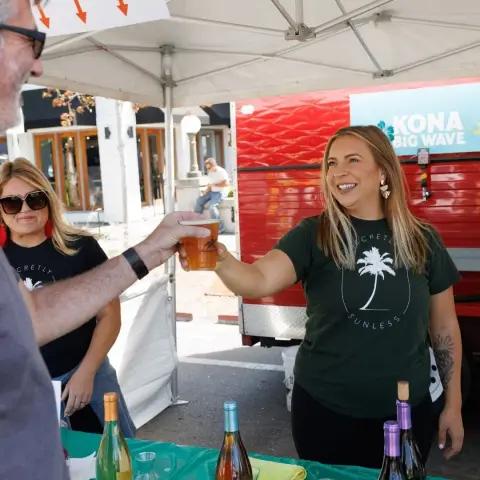 A smiling woman serving a drink at an outdoor booth.