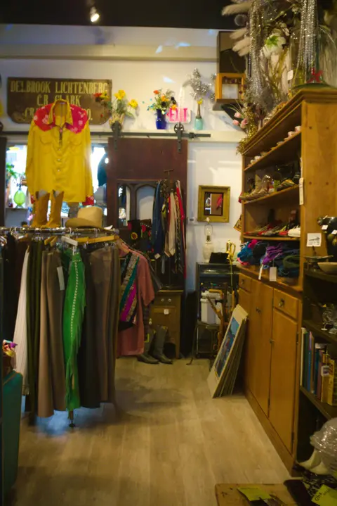 An interior view of a clothing and vintage store with racks of garments and wooden shelves.