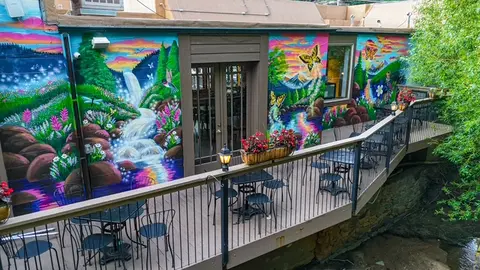 An outdoor balcony with tables and chairs alongside a colorful mural.