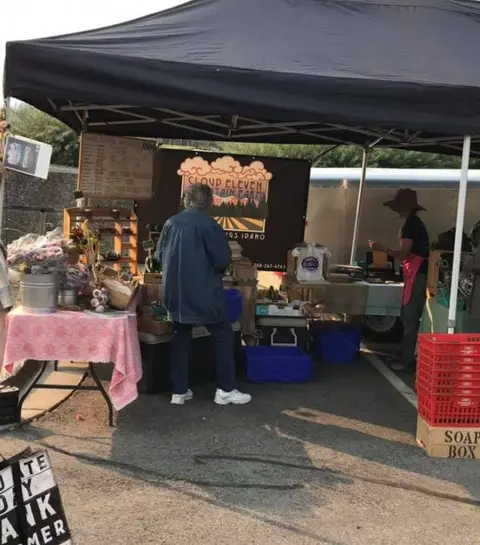 A vendor tent at an outdoor market with produce and goods.