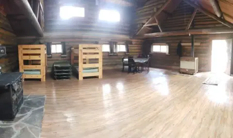 Inside a spacious rustic log cabin with wooden bunk beds and a stove.