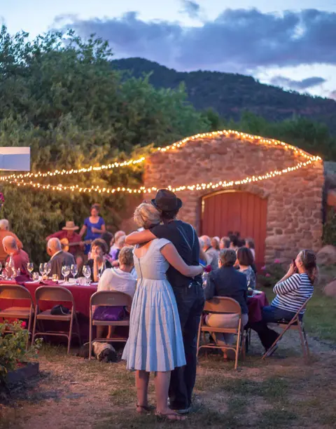 A couple dancing outdoors at an evening gathering with string lights.