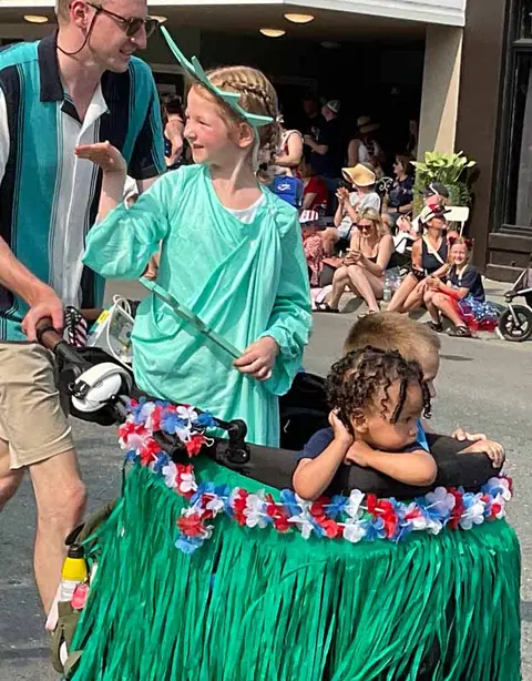 A child in costume walks near a decorated stroller during an outdoor event.