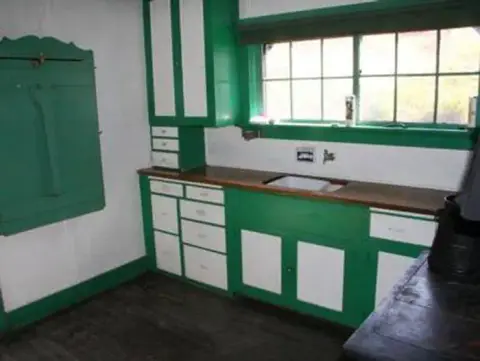 An interior view of a historic kitchen with green and white cabinets.