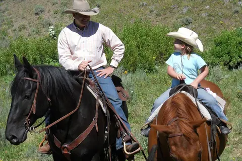 A man and a child ride horses outdoors.