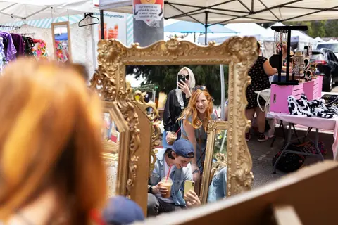 People look into decorative mirrors at an outdoor market.